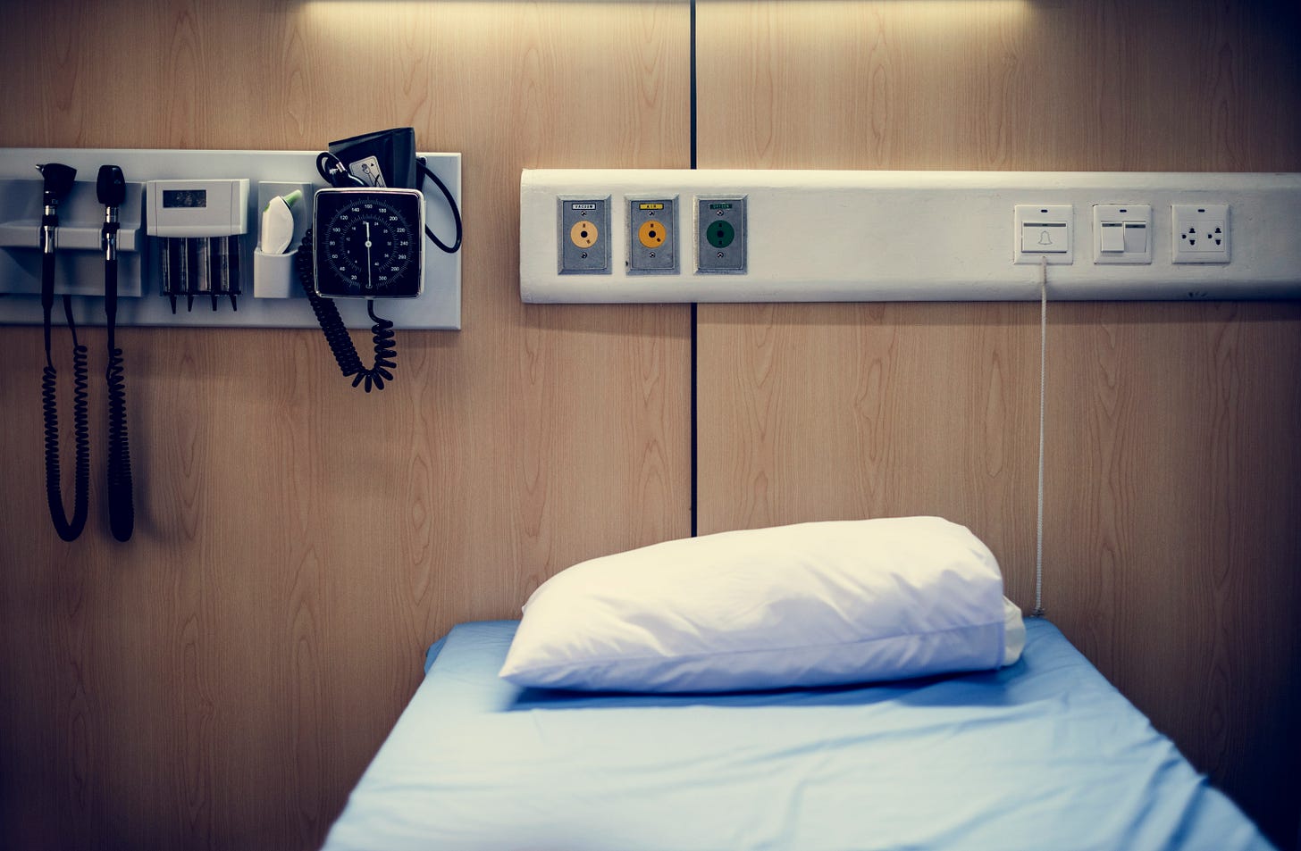 a hospital room with a brown wood wall and a bed with blue sheets. 