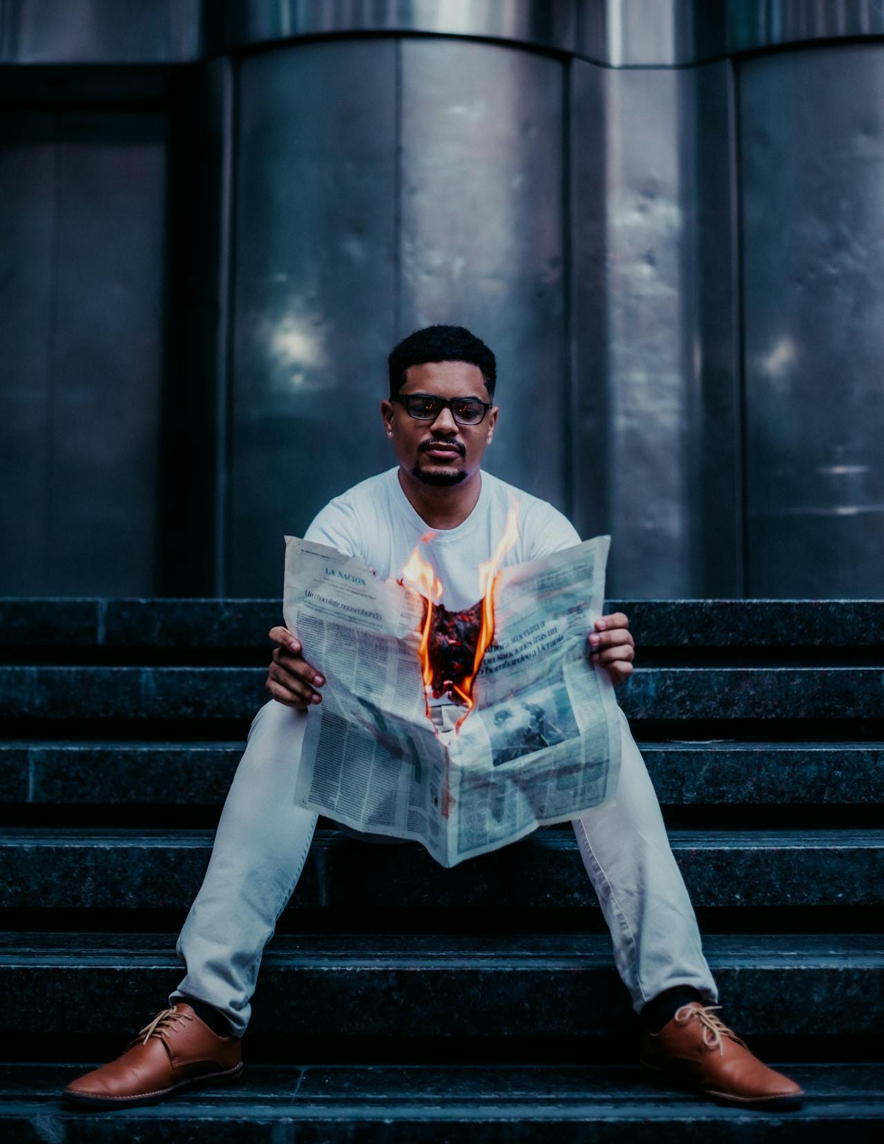 A brown-skinned man reading a newspaper on fire.