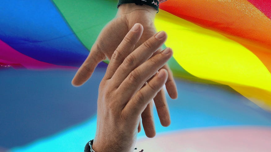 Image of two hands embraced against the background of a raindow pride flag