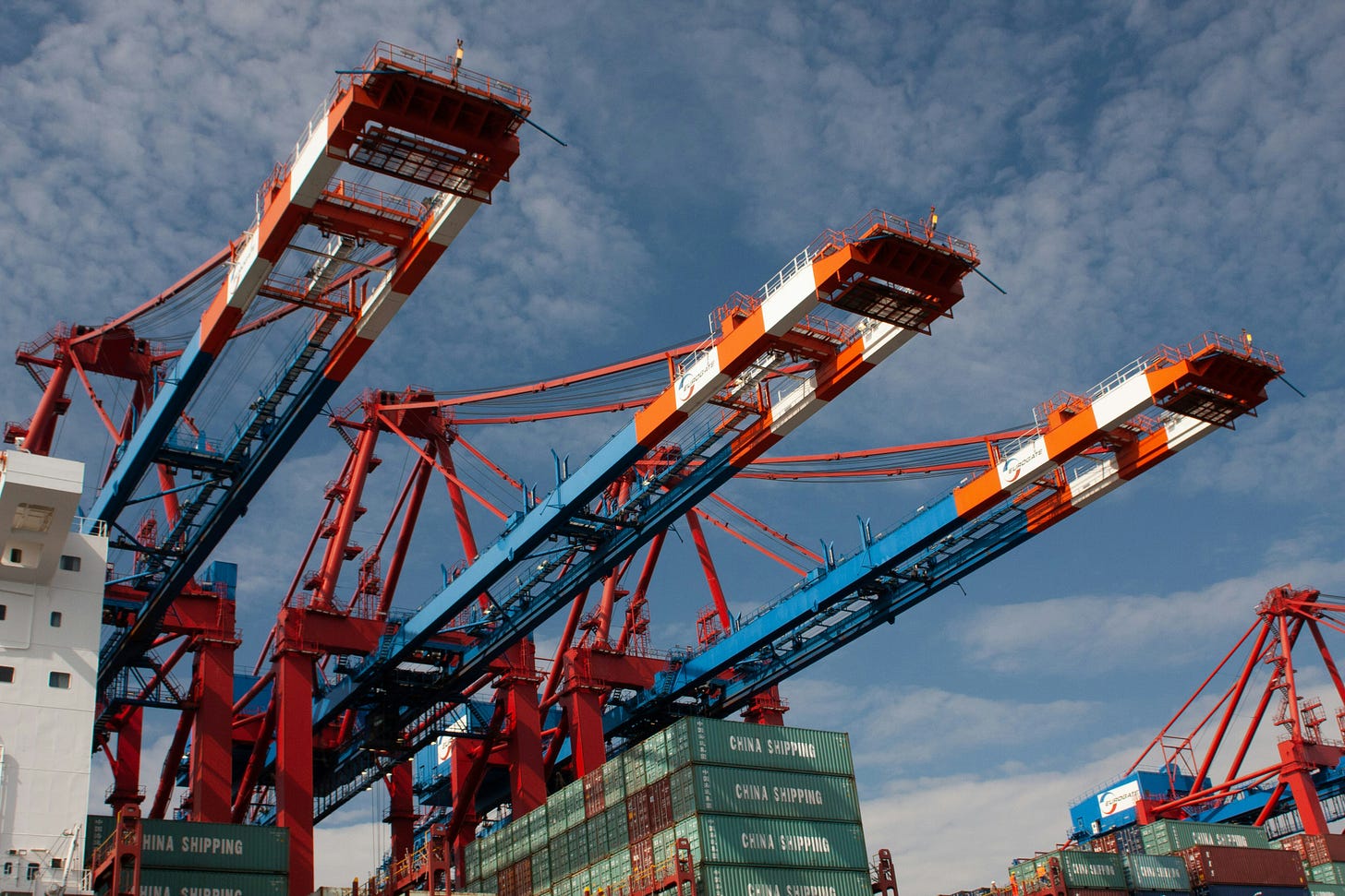 Red and white container cranes loading China Shipping containers at busy port terminal under cloudy sky