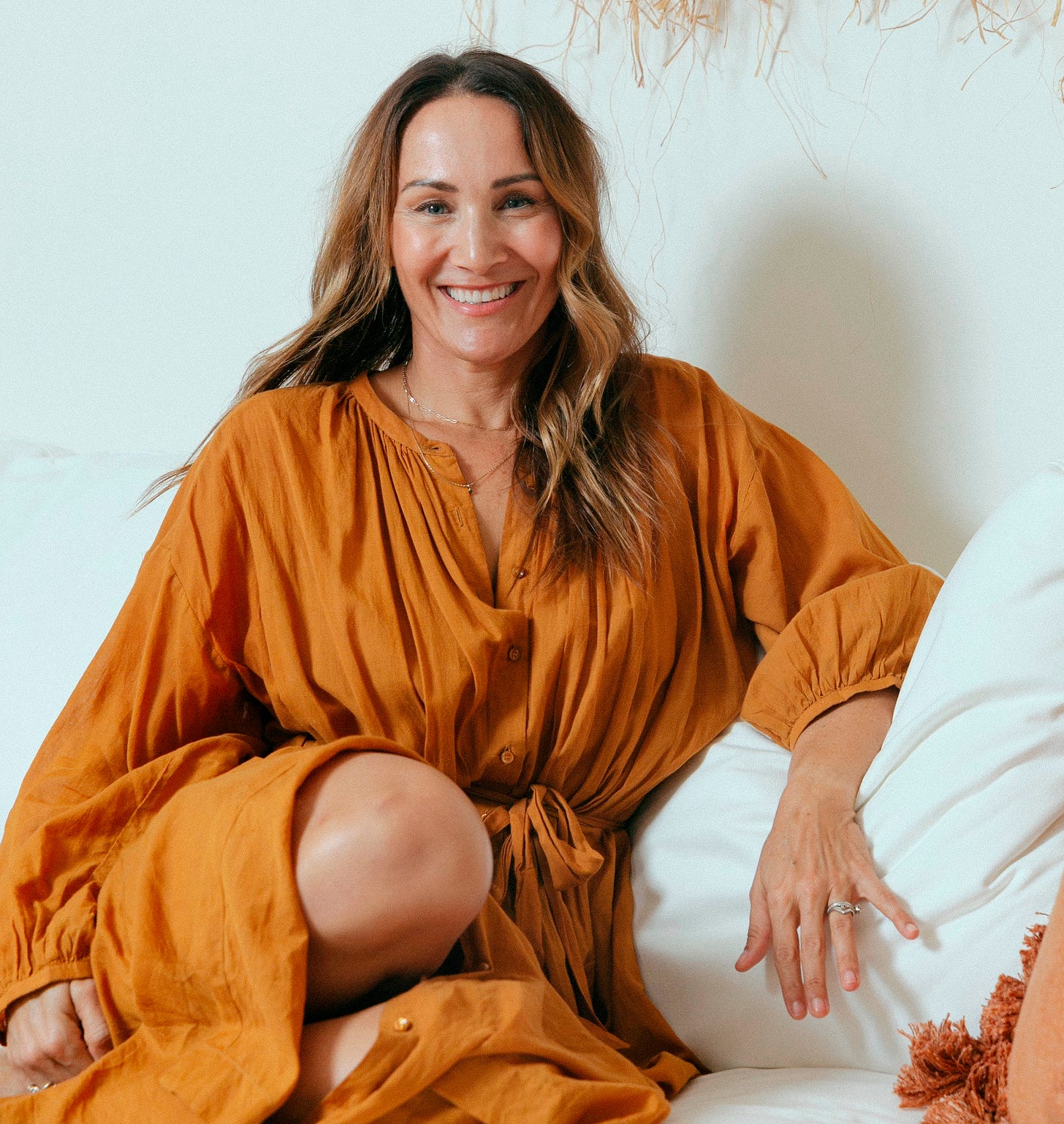 Smiling woman with long hair, wearing an orange dress against a white background