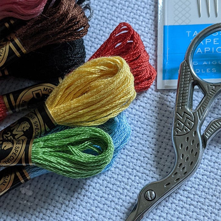 Stitching supplies in a close-up photograph. It shows floss skeins, stork scissors and a pack of tapestry needles. Stitching supplies in a close-up photograph. It shows floss skeins, stork scissors and a pack of tapestry needles.