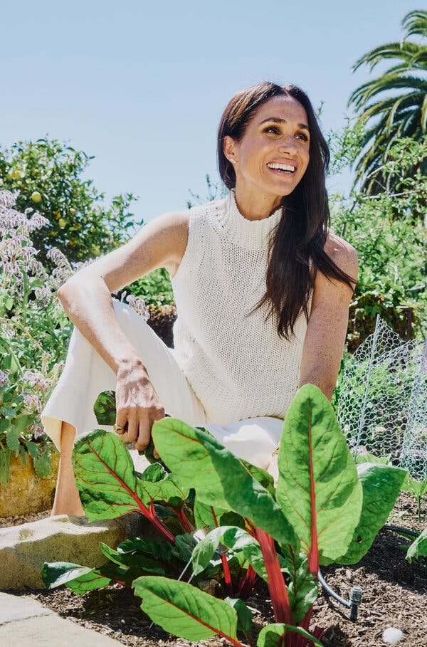 Meghan, Duchess of Sussex, smiles and leans over a garden patch of sprouting leafy greens.