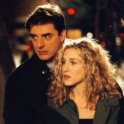 This may contain: a man and woman standing next to each other on a street at night with lights in the background This may contain: a man and woman standing next to each other on a street at night with lights in the background