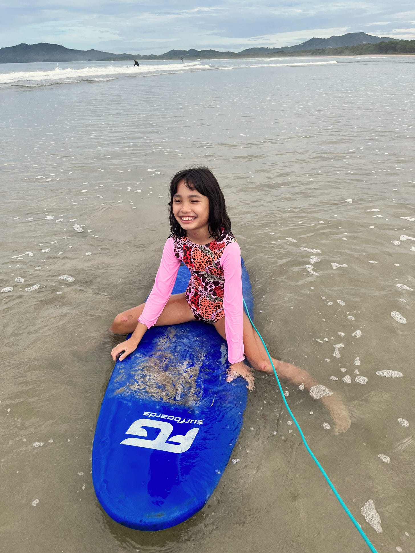 Girl sitting on surfboard in shallow ocean water.