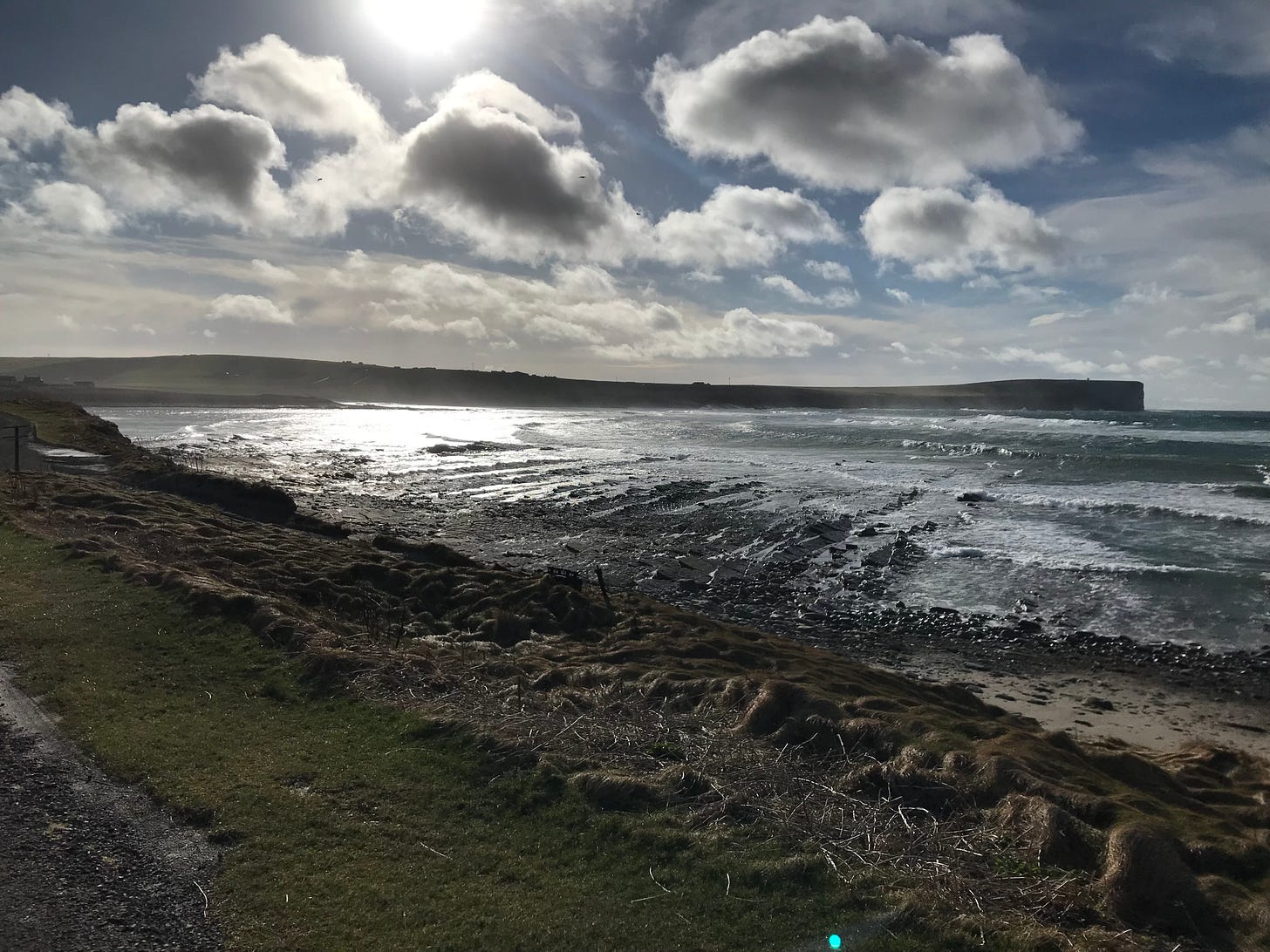 silvery sunlight over a wide bay with a dark headland beyond
