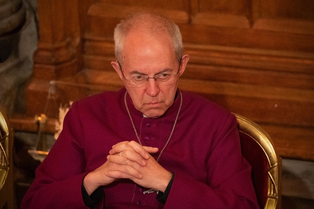 The Archbishop of Canterbury wears a red robe and sits with his hands folded.