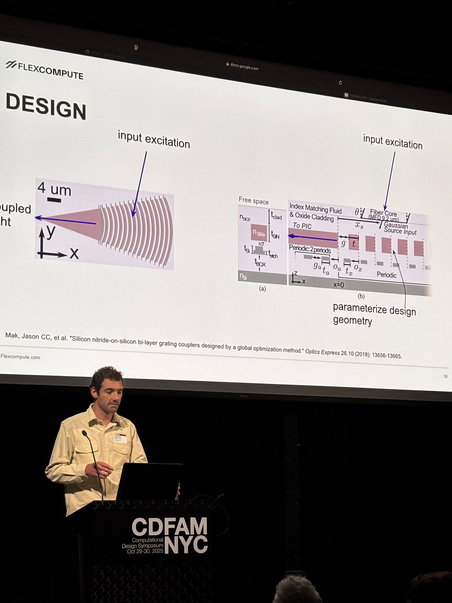 A male presenter stands behind a podium at a conference, discussing design optimization methods, with diagrams displayed on a screen behind him, illustrating input excitation and design geometry parameterization. A male presenter stands behind a podium at a conference, discussing design optimization methods, with diagrams displayed on a screen behind him, illustrating input excitation and design geometry parameterization.