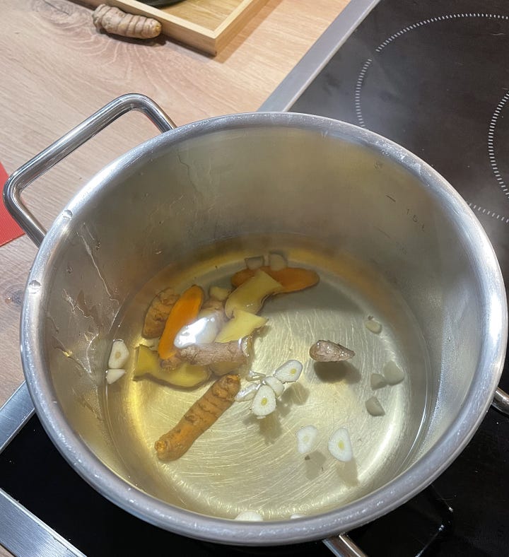 Left: A small pot with garlic, ginger slices, and turmeric slices being brought to a boil. Right: A cup of green tea infused with cayenne powder and the ginger/turmeric water from the pot on the left.