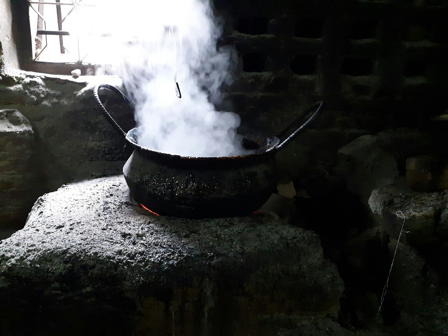 An old cauldron sits on a stone hearth in a decaying room, emitting clouds of white smoke.