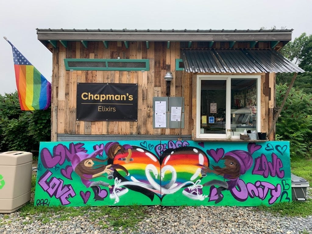 The order window of Chapman's Elixirs. A rain box flag on the left. A mural painted accross the bottom with the words love and unity. The order window of Chapman's Elixirs. A rain box flag on the left. A mural painted accross the bottom with the words love and unity.