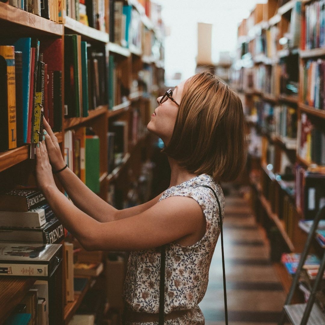 woman standing between library book shelves woman standing between library book shelves