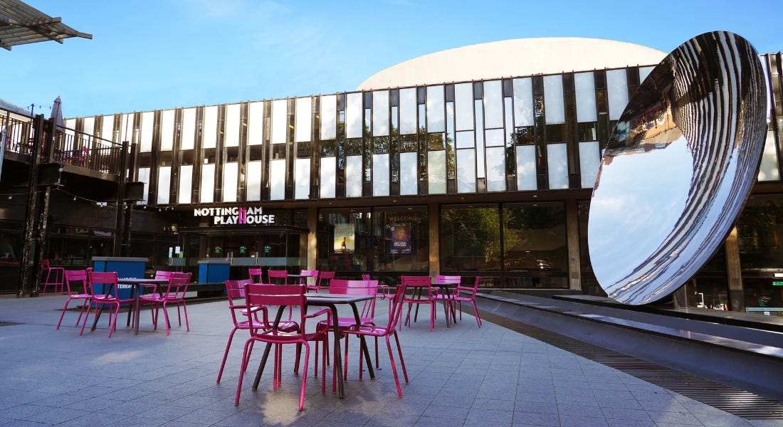 A theatre with mirrored panels, a large mirror circle sculpture, and pink dining seats in front of it A theatre with mirrored panels, a large mirror circle sculpture, and pink dining seats in front of it