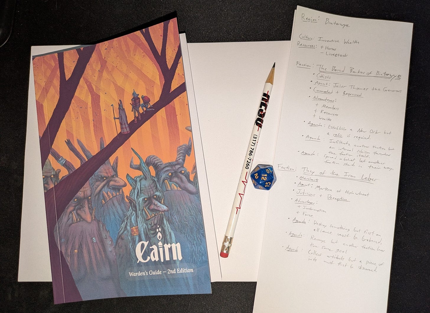 The Cairn 2e Wardens Guide, printer paper, a pencil, a D20, and a partially completed list of notes about a region named Bintarwye and two factions, the Barred Bankers of Bintarwye and They of the Iron Ledger. 