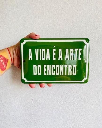 This may contain: a hand holding a green sign that says, a via e arte do encontro