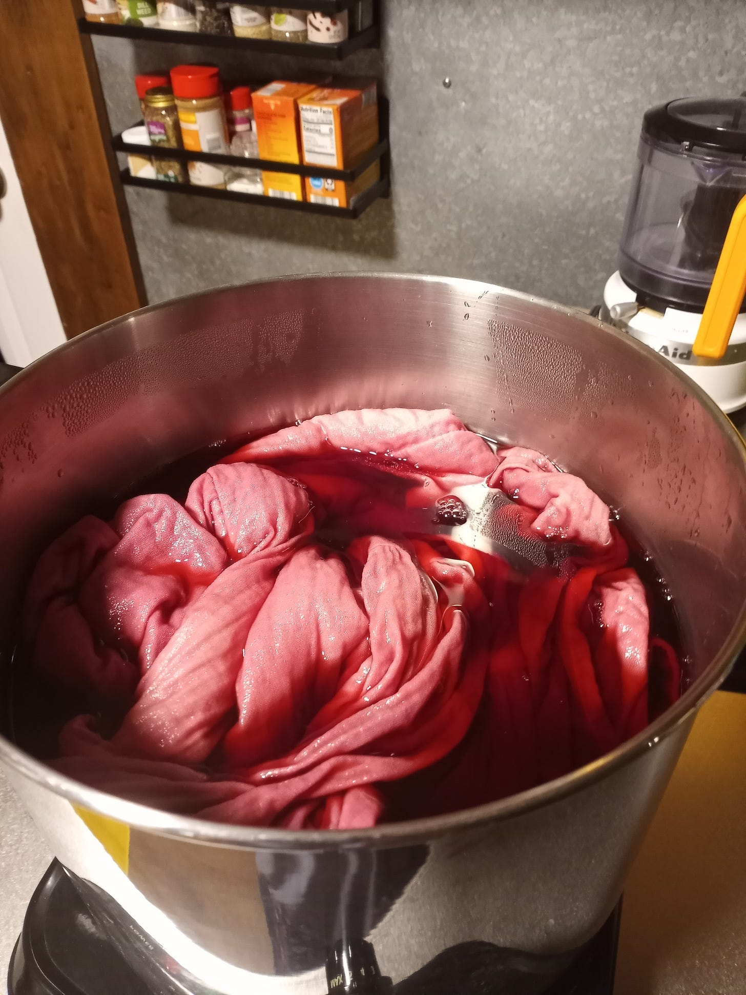 A white dress sits in a pot of grape juice, on a burner. The dress is turning pink.