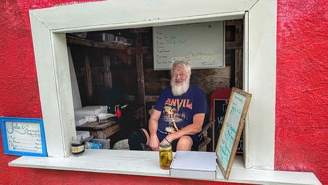 From left to right: a photo of a red shack beside a country road with a sandwich board outside. There's a little window in the side of the shack with a counter. Next, a photo of a man with a large white beard in the shack. There are containers of butter tarts surrounding him. On the counter there is a jar of pickles and a price list. Finally, there is a shot of an open box containing the butter tarts and jar of pickles we bought.