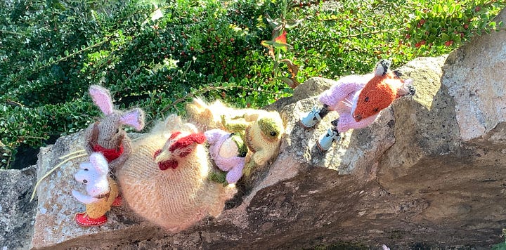 Knitted toys atop a stone wall with foliage in the backgroud