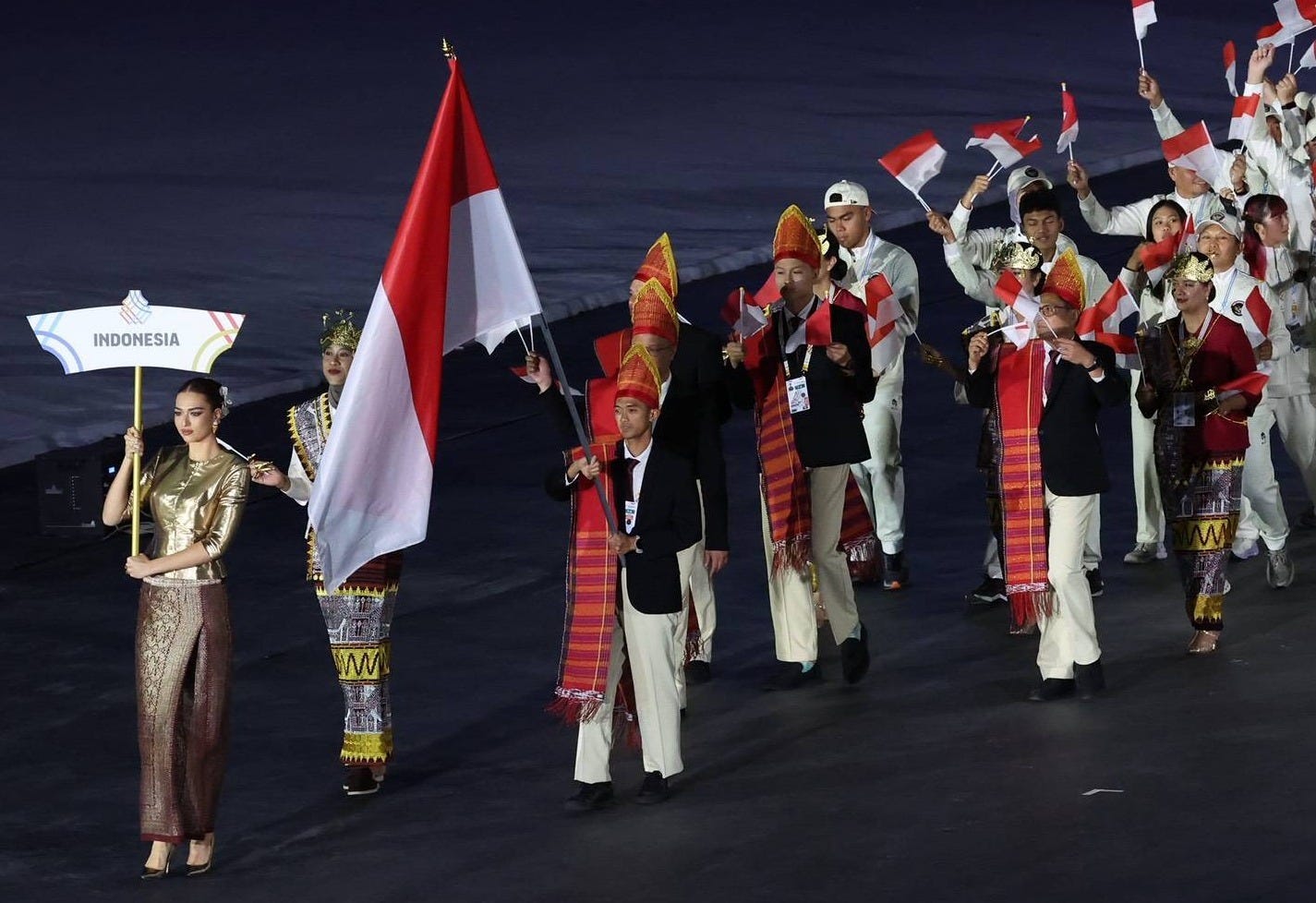 A group of athletes in regional clothing and official uniforms waved Indonesian flags and a woman carried a sign that said Indonesia. A group of athletes in regional clothing and official uniforms waved Indonesian flags and a woman carried a sign that said Indonesia.