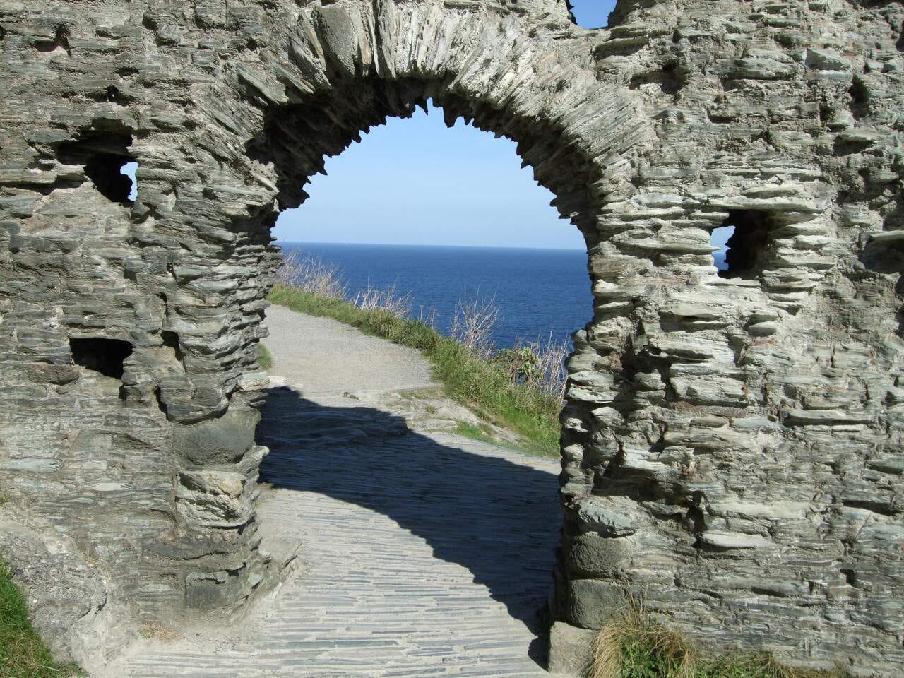 A doorway in an old stone wall with a path leading to a cliff overlooking the sea