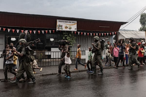 Rebels carrying weapons om a city street as people look on.