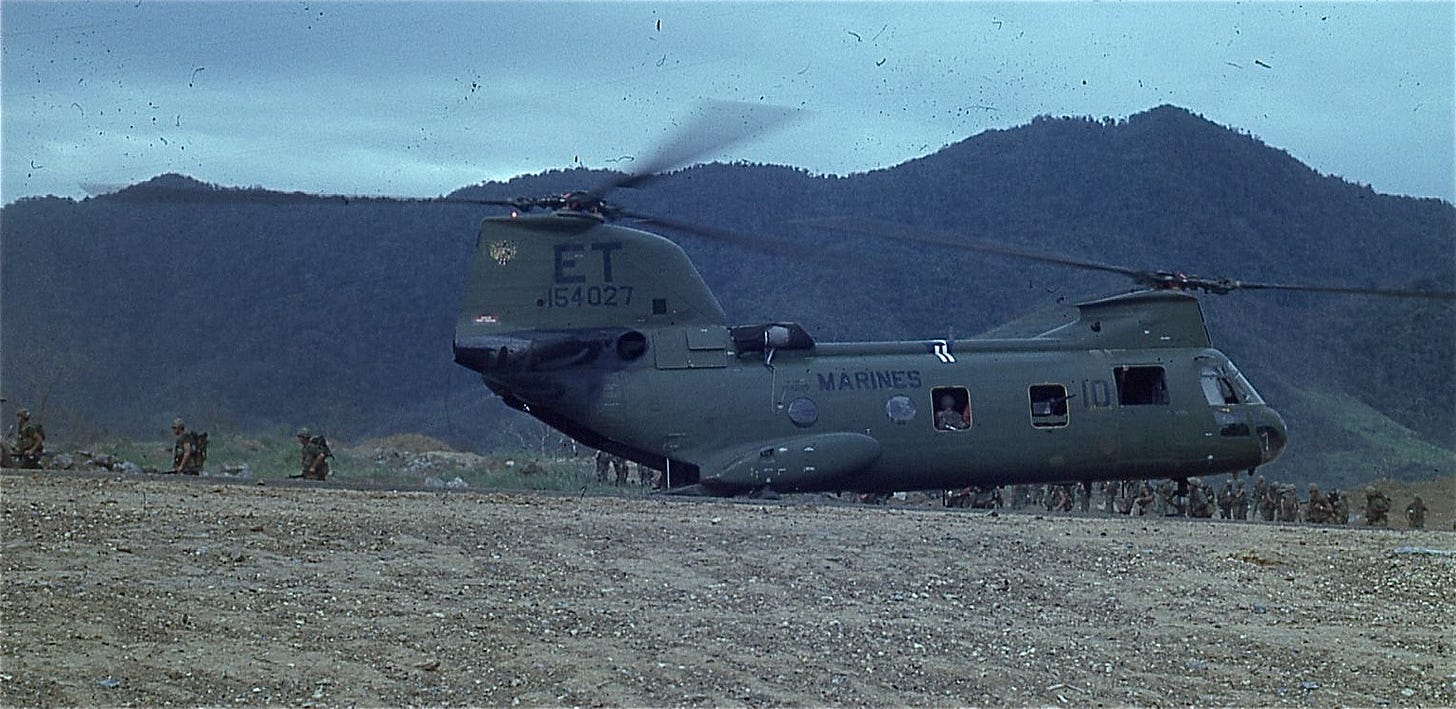 CH-46 helicopter loading infantry Marines in Vietnam, with a mountainous backdrop.