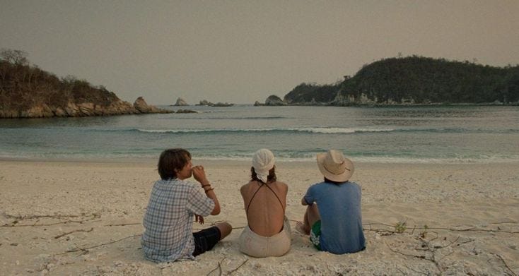 This may contain: three people sitting on the beach looking out at the water