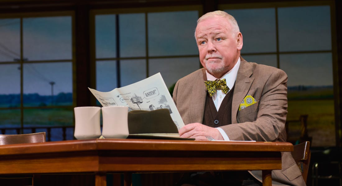 A man wearing a brown blazer sat at a desk holding a newspaper A man wearing a brown blazer sat at a desk holding a newspaper