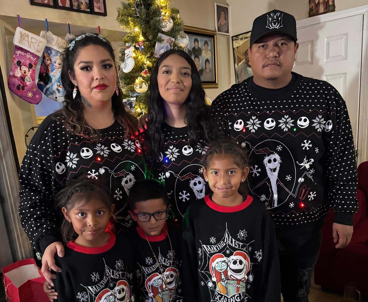 A family of six wearing matching sweaters poses for a photo in front of a Christmas tree and stockings A family of six wearing matching sweaters poses for a photo in front of a Christmas tree and stockings