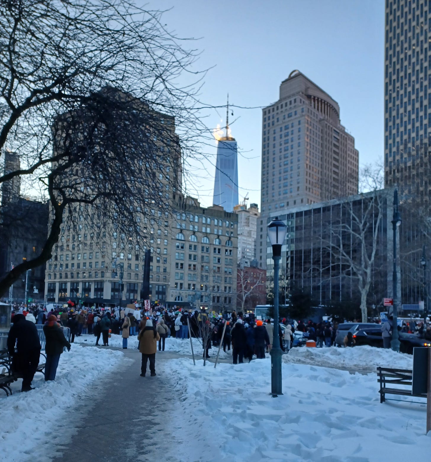 The Freedom Tower stands over a snowy plaza with a crowd protesting murders by ICE in New York City, January 30, 2026.