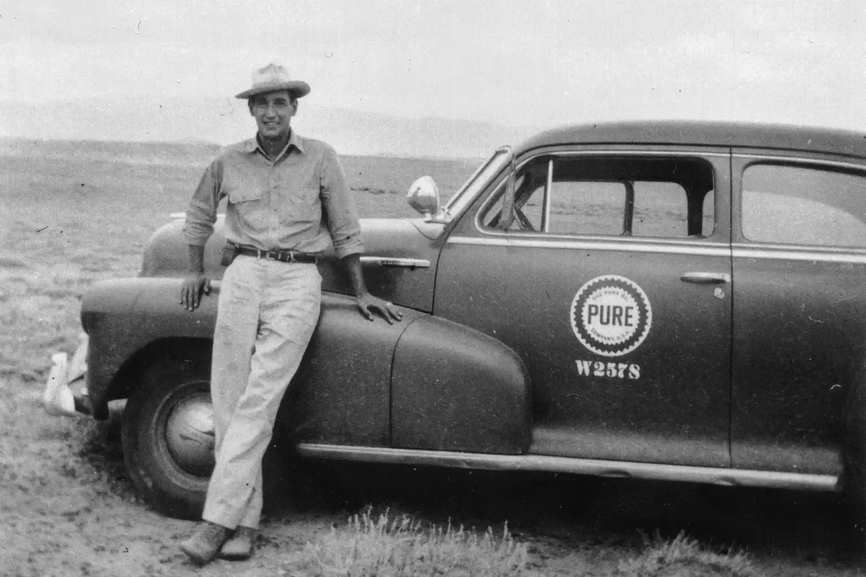 Black and white photo of a geologist leaning against a car