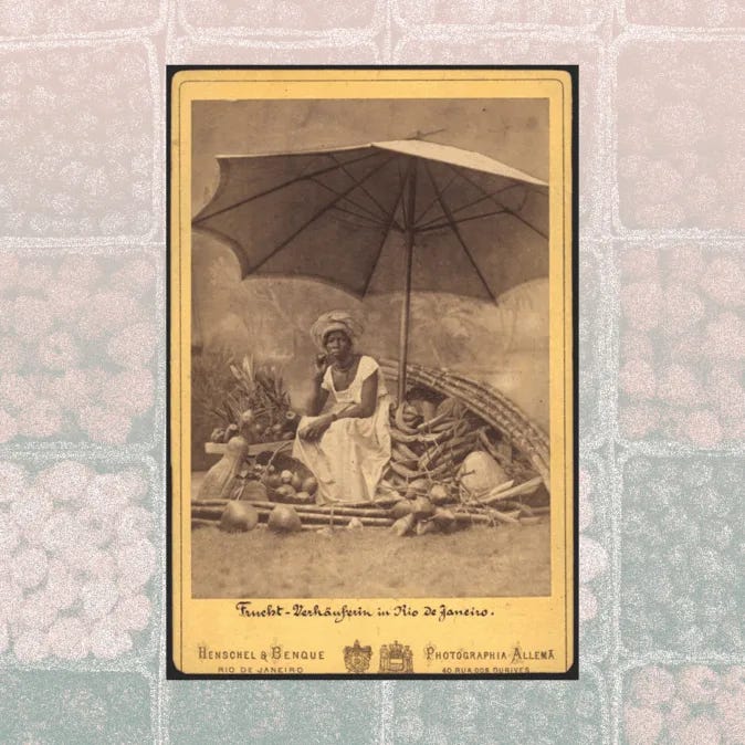 Fotografia antiga de uma vendedora de frutas no Rio de Janeiro. A mulher está sentada sob um grande guarda-sol, cercada por cestos cheios de frutas tropicais. Ela veste roupas brancas e um turbante, com uma expressão serena. Fotografia está em uma moldura preenchida por padrões de frutas estilizadas.