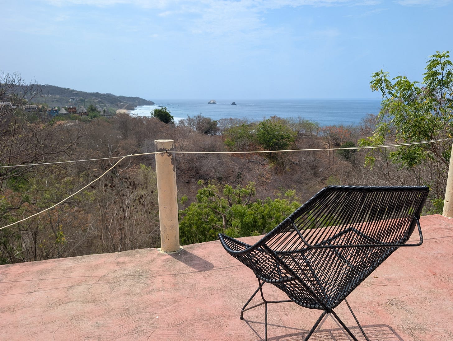 a black woven chair on a concrete terrace overlooking a coastal landscape and blue ocean