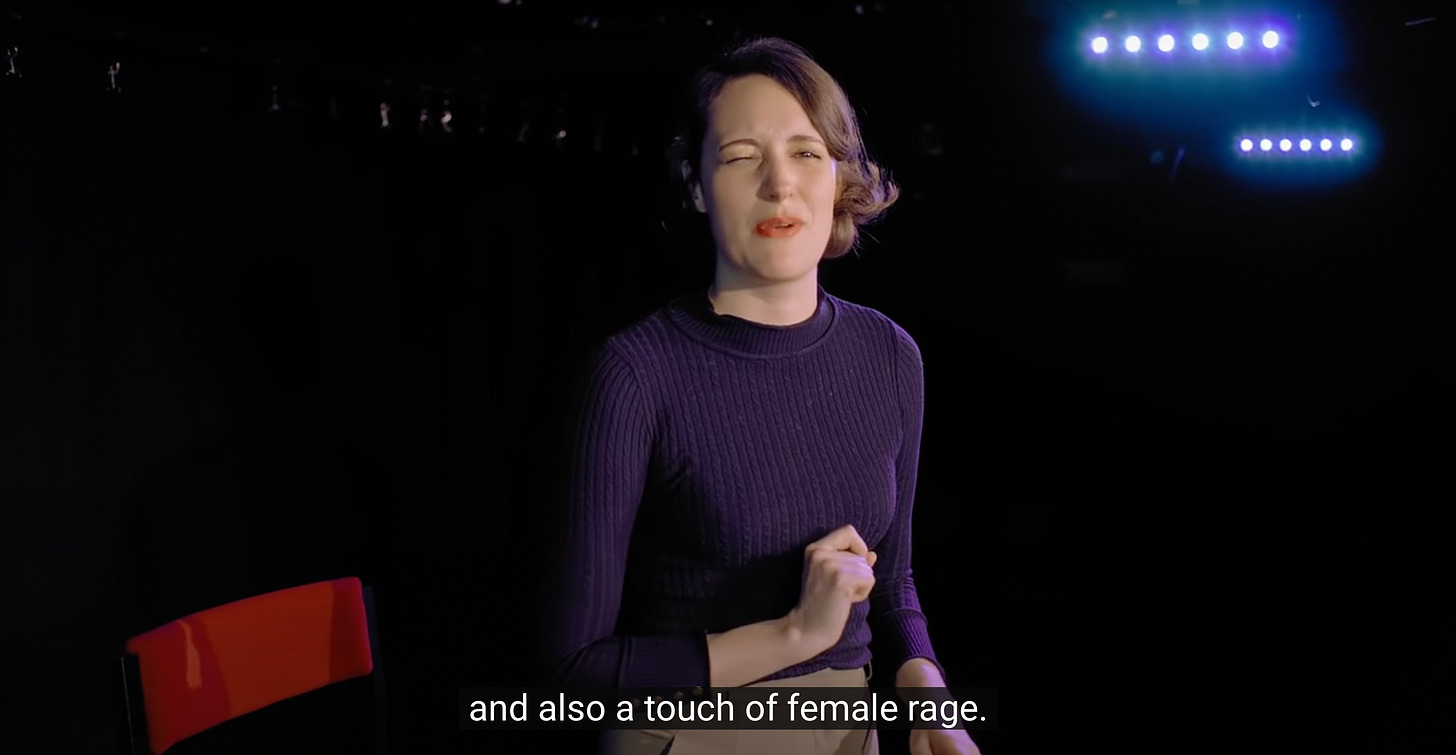 A screenshot from the "73 Questions With Phoebe Waller-Bridge" Vogue video interview. She is in a theatre, against a minimal black background, wearing a black shirt. She is squinting at the camera while saying the words in the subtitle, which are "and also a touch of female rage."