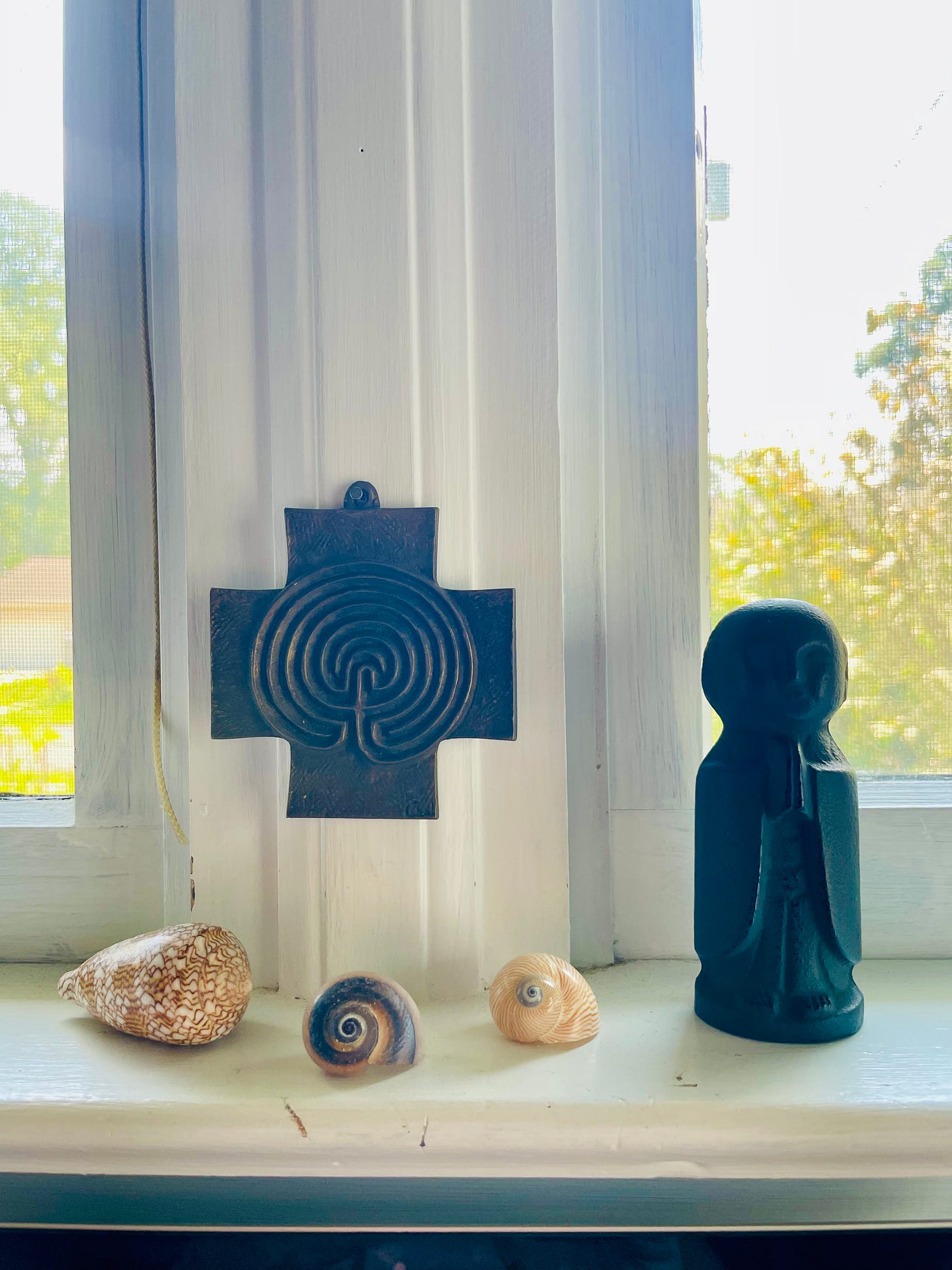 alternate description: a windowsill and windowframe; a metal cross hangs in the left center; three shells are placed under the cross on the sill; a bodhisattva statue prays on the sill to the right of the shells