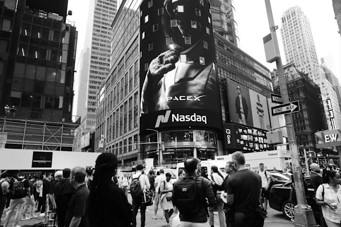 A large crowd gathers in Times Square beneath a Nasdaq billboard displaying a SpaceX astronaut visual after the company’s IPO launch