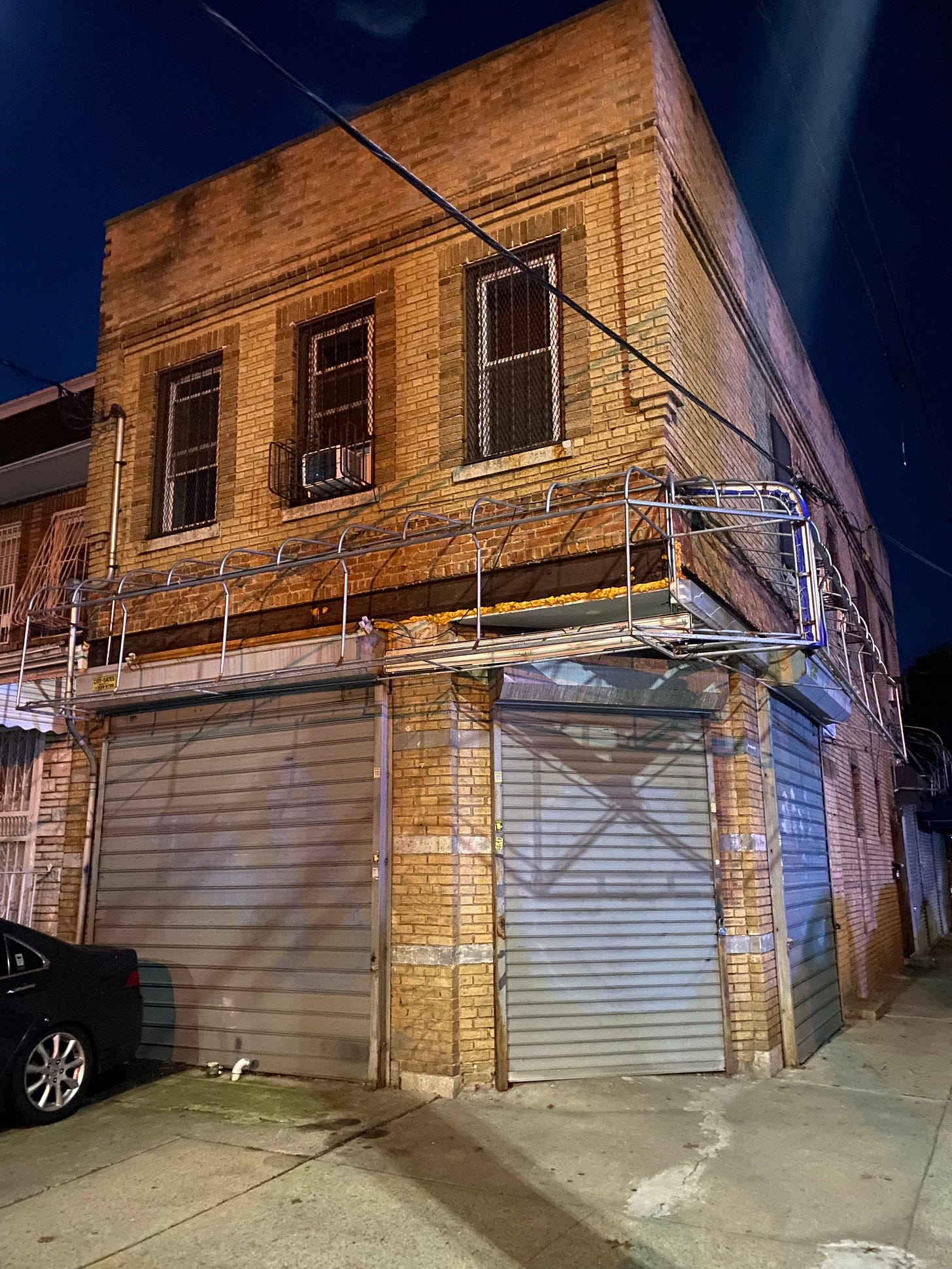 Image shows a recent photograph of the corner of 91st Avenue and 84th Street in Woodhaven. The storefront is no longer in use. A car sits on the concrete in front of it.