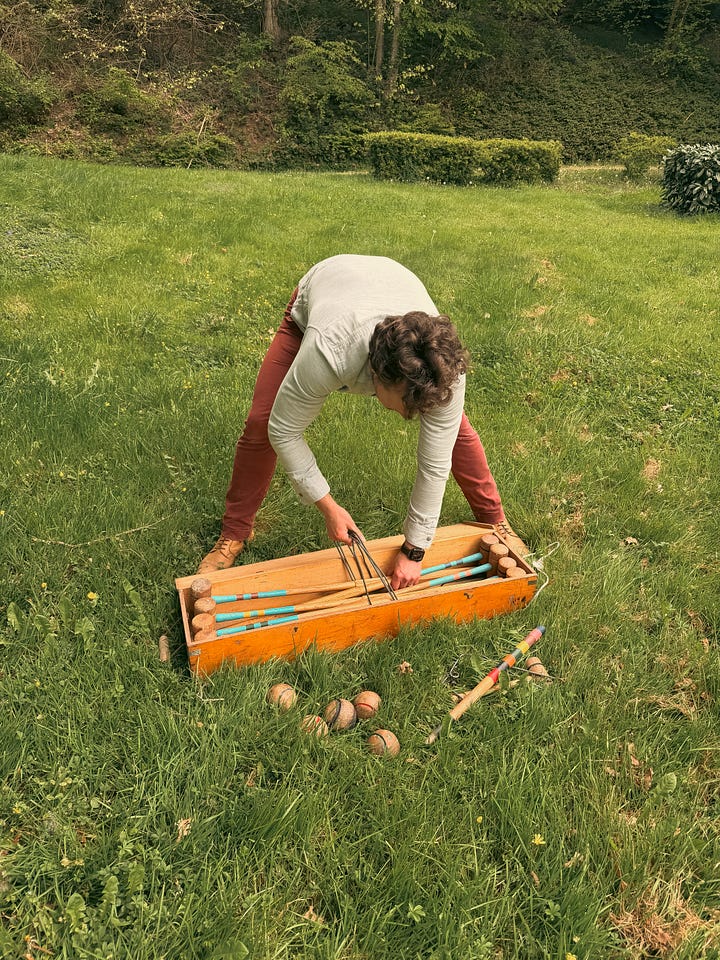 Man opening antique croquet set and woman playing croquet on a château lawn