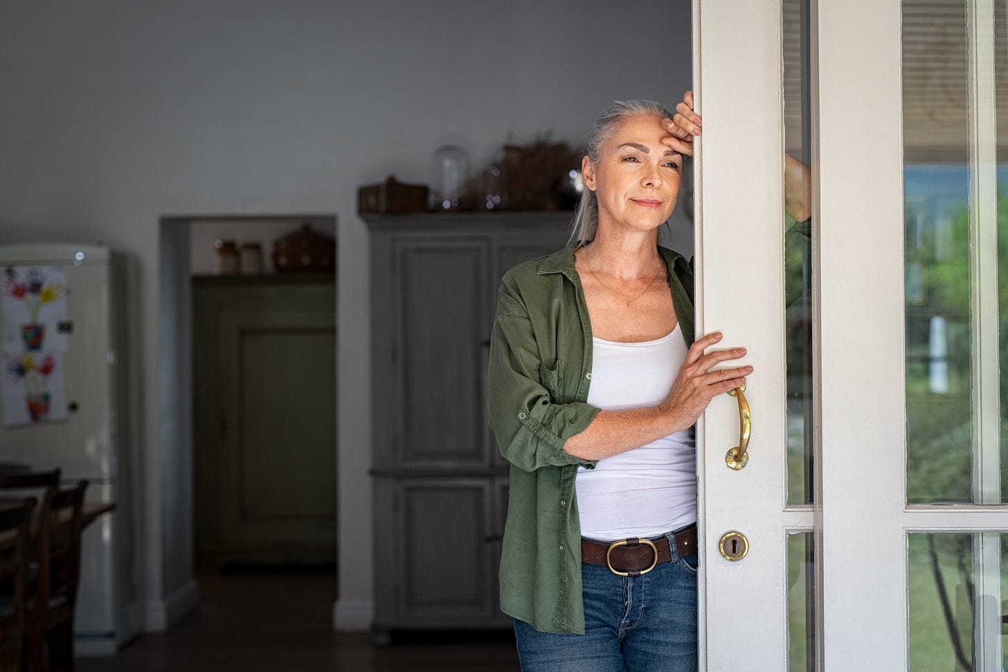 A woman with silver hair smiles and stares hopefully out of a patio door. A woman with silver hair smiles and stares hopefully out of a patio door.