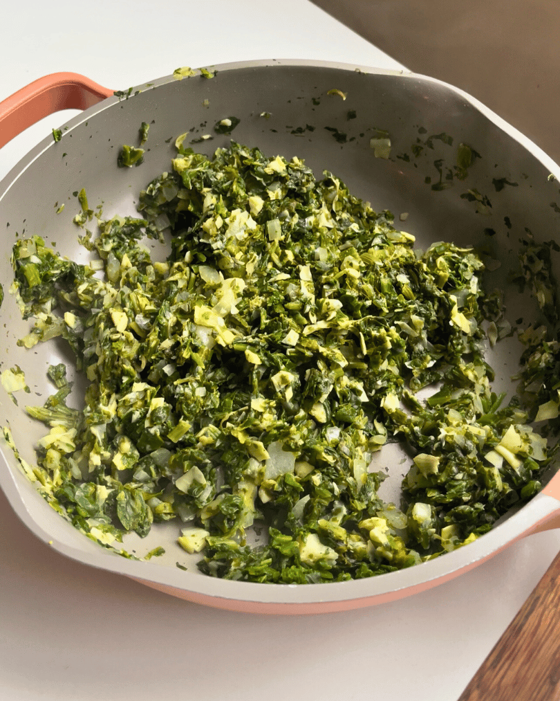 spinach, artichoke and onion being cooked in a pink pan