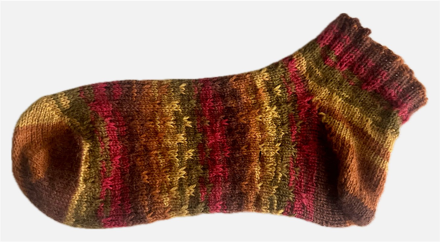 A multicoloured striped sock with a slip-stitch pattern on the foot, lying on its side.