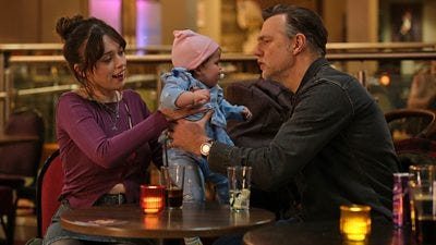 A young woman carefully passes a baby across a table in a bar to an older man.
