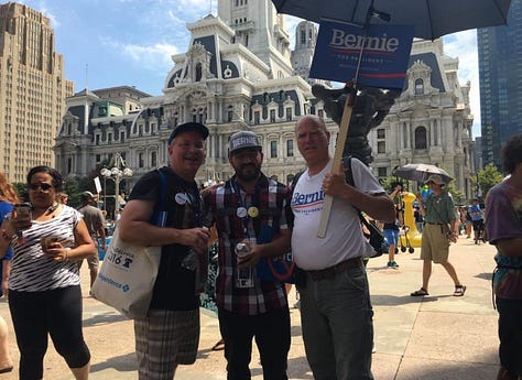 Kacey Carpenter holding signs, wearing shirts, buttons, and voting for Bernie Sanders as DNC delegate in Philly in 2016