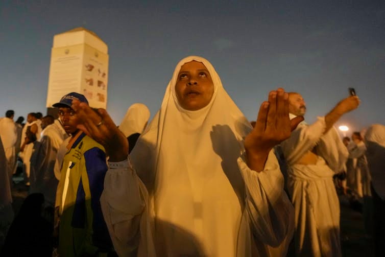 A woman with her head and neck covered holds up her hands as she looks toward the sky. A woman with her head and neck covered holds up her hands as she looks toward the sky.