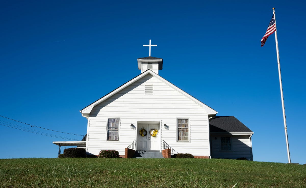 White church with a cross on top and a U.S. flag on a flagpole in the church's lawn White church with a cross on top and a U.S. flag on a flagpole in the church's lawn