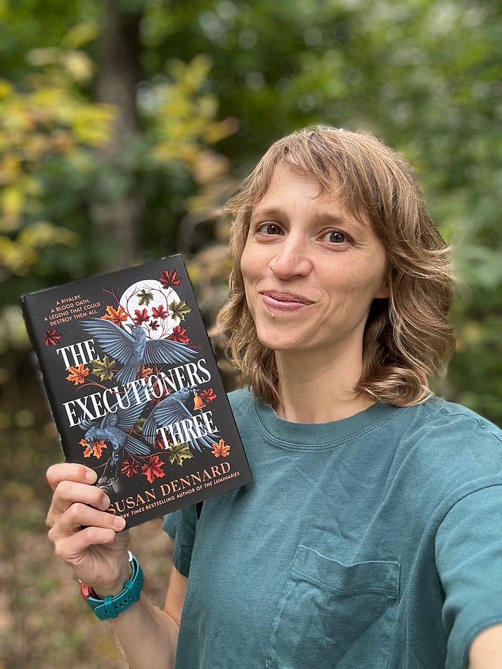 Four photos of Sooz with The Executioners Three in front of the first autumn leaves of the season. In the first photo, she's smiling, in the second she's looking goofily afraid, in the third she's showing the printed edges that read Take Heed, and in the fourth, she's showing the gorgeous end papers that show the full color map