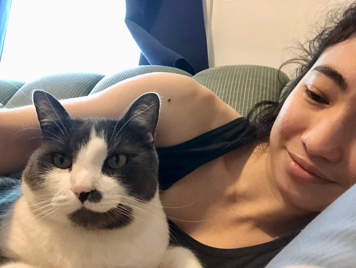 A grey and white tuxedo cat curled up next to a smiling person.