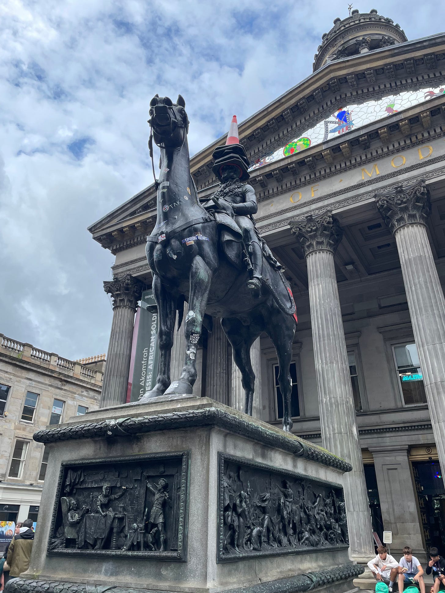 A statue of a man on horse outside the Glasgow Museum of Modern Art. The rider has several traffic cones on his head.