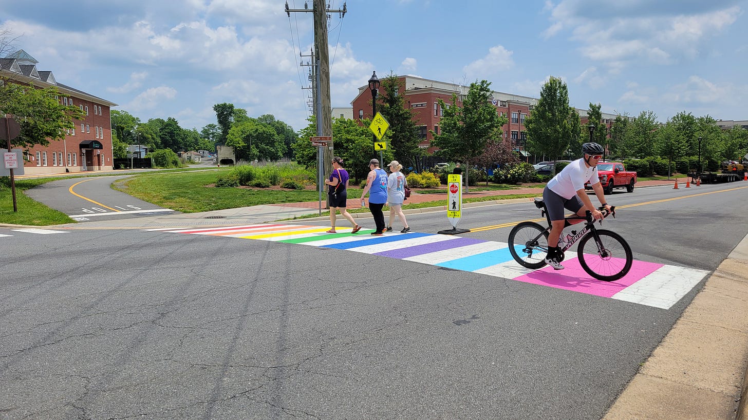 Community members crossing at a rainbow crosswalk while another rides a bike