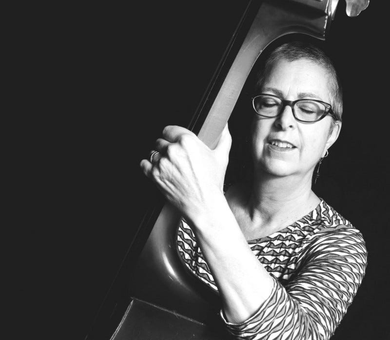 Woman with cropped hair playing upright bass with eyes closed.